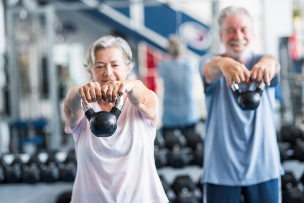pareja de dos personas mayores activas y saludables o jubilados o personas maduras haciendo ejercicio juntos en el gimnasio sosteniendo una pesa en sus manos y haciendo sentadillas - concepto de dieta de estilo de vida fitness